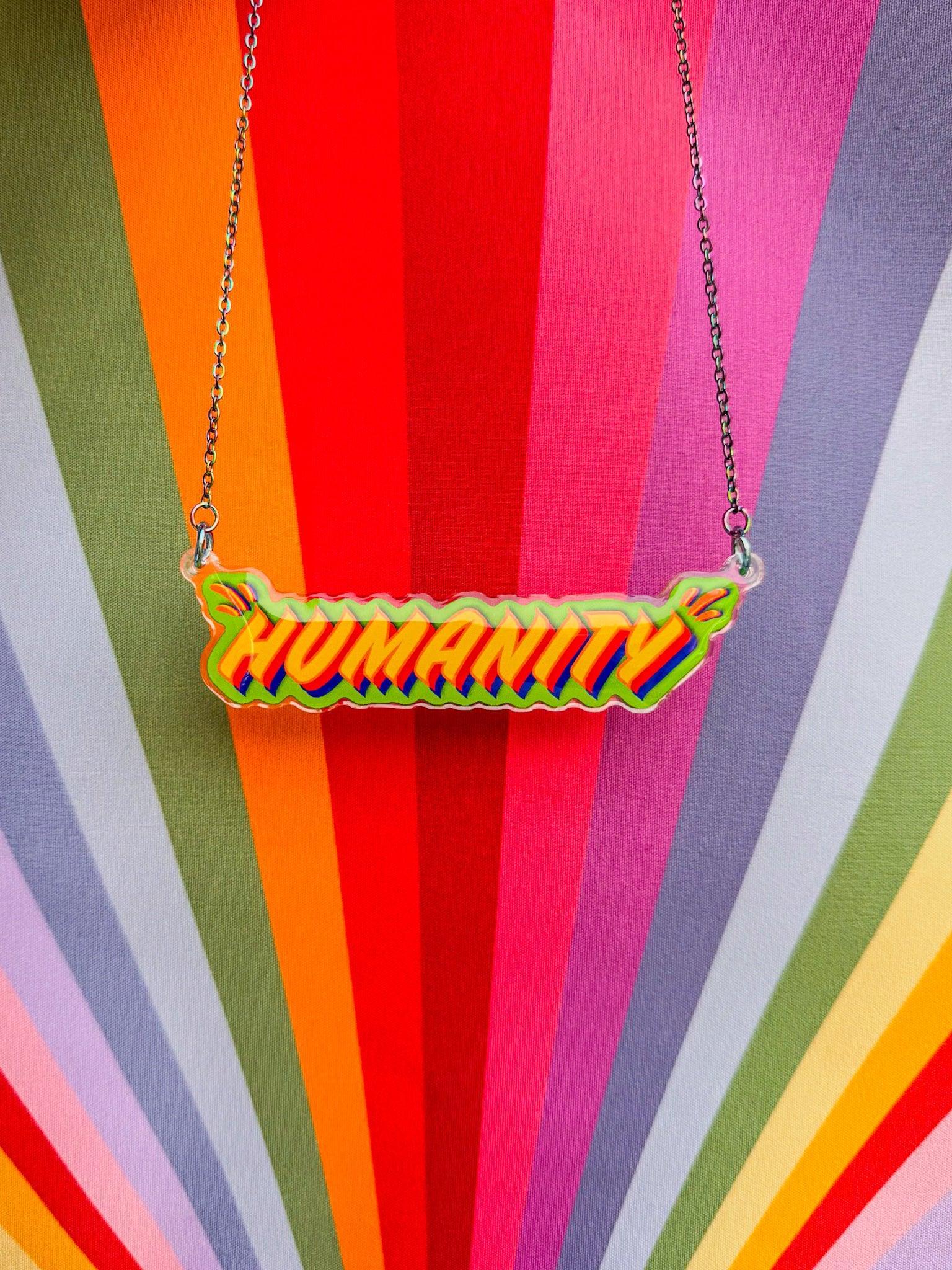 'HUMANITY' necklace on a colourful striped background - a jewellery piece from Stoofy’s Primary Comcerns Original Art Collection - designed by UK mixed media artist Stoofy. 