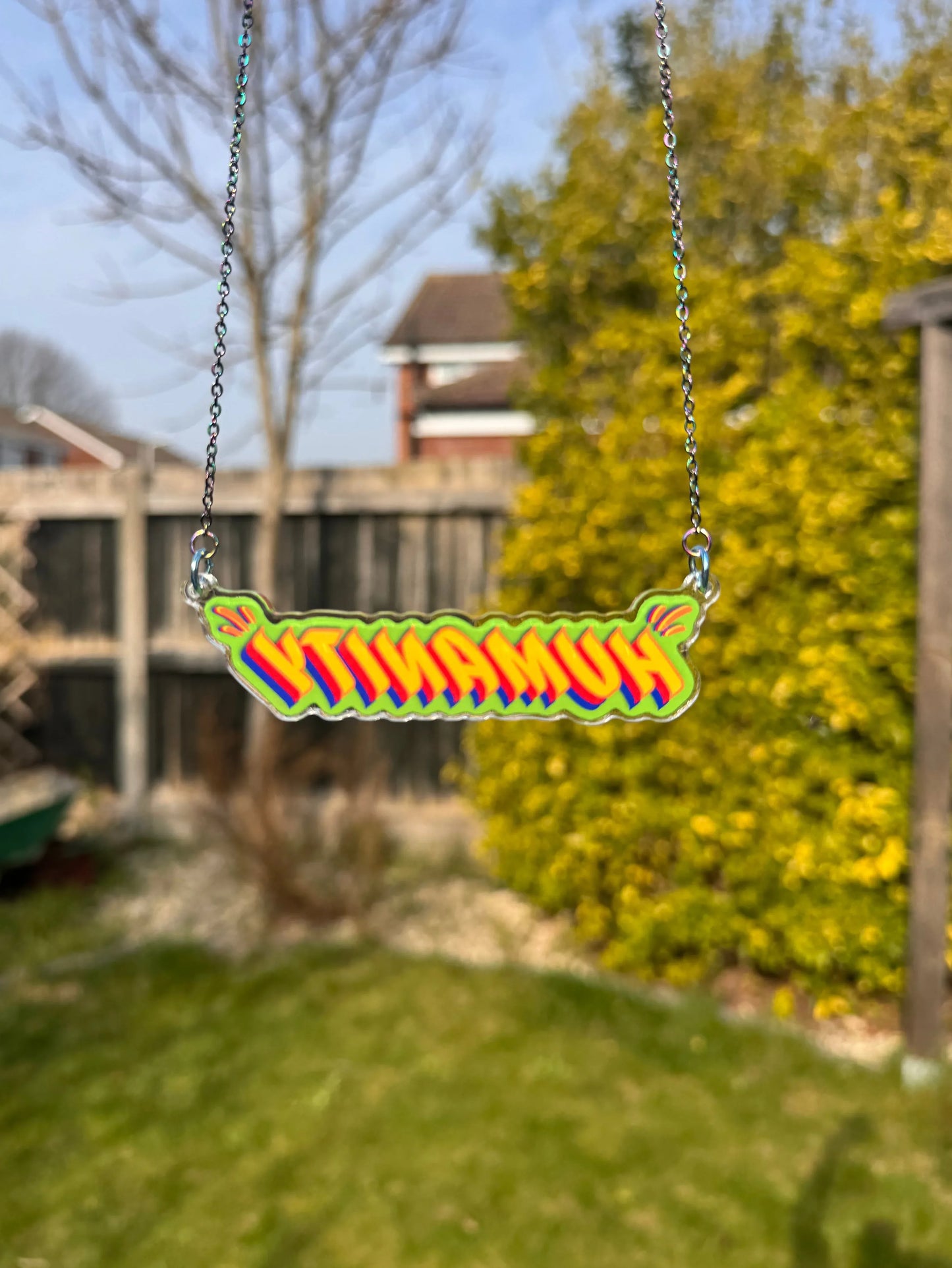 Colourful ‘Humanity’ pendant necklace by Stoofy  against a blurred outdoor background.