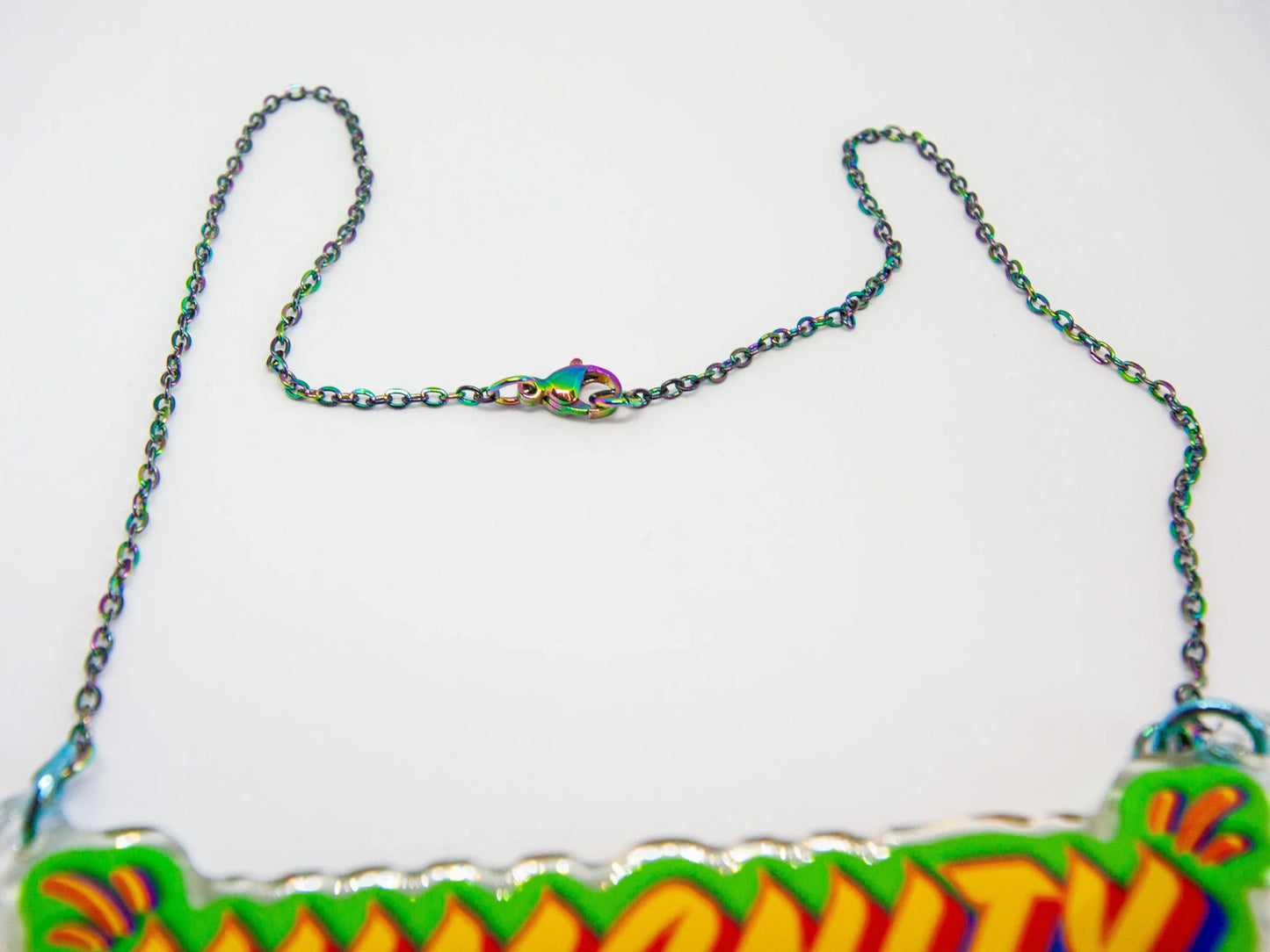 Close up of stainless steel oil slick chain and clasp with colourful 'HUMANITY' pendant on a white background by UK artist, Stoofy. 
