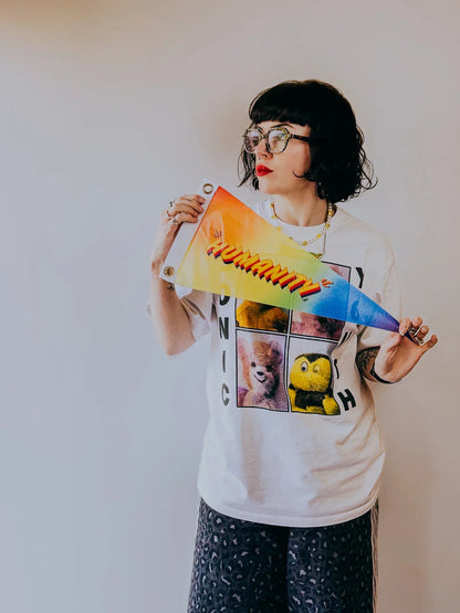 Artist Stoofy holding colourful ‘Humanity’ pennant flag against a plain background. Design and copyright by Stoofy