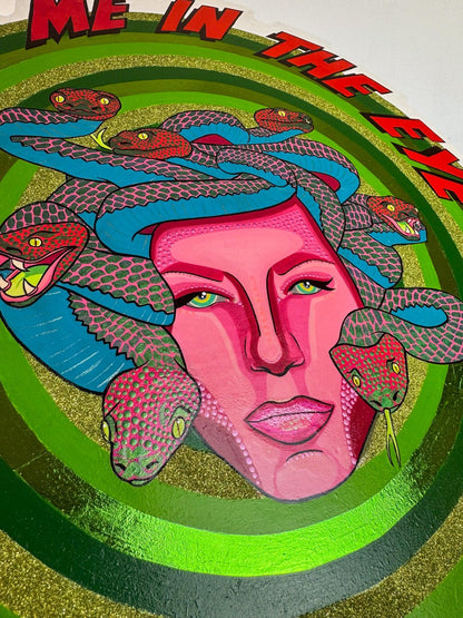 Close detail of Look Me in the Eye — Tell Me to Smile! by Stoofy, showing the full face of Medusa and the surrounding snake composition. Magenta pink face with Ben-Day dot forehead, strong brow line and green-gold eyes, expression completely calm. Blue, red-pink and dark green snakes with individually painted scales fill the space around her head. Gold-green glitter concentric rings visible at the edges. Original mixed media on hand-cut shaped wood panel.